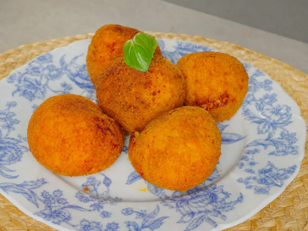 Arancini – frittierte Reisbällchen mit Basilikum auf blau-weißem Teller