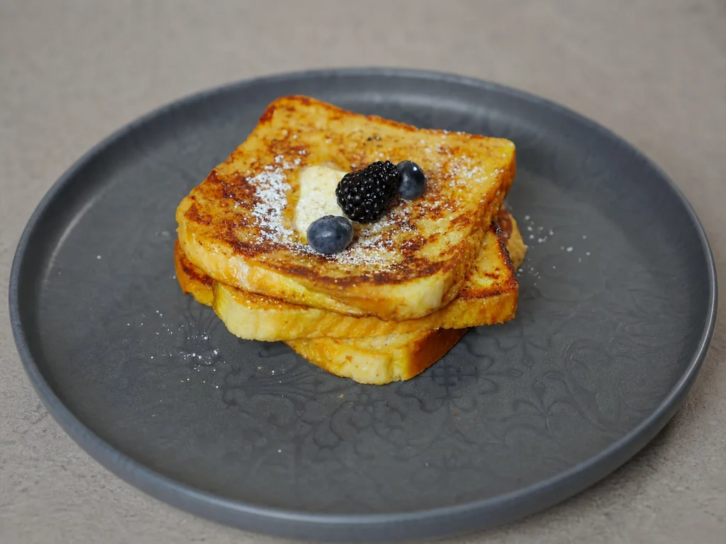 Arme Ritter – goldbraun gebratene Toastscheiben mit Puderzucker, Zimt und frischen Beeren auf dunklem Teller