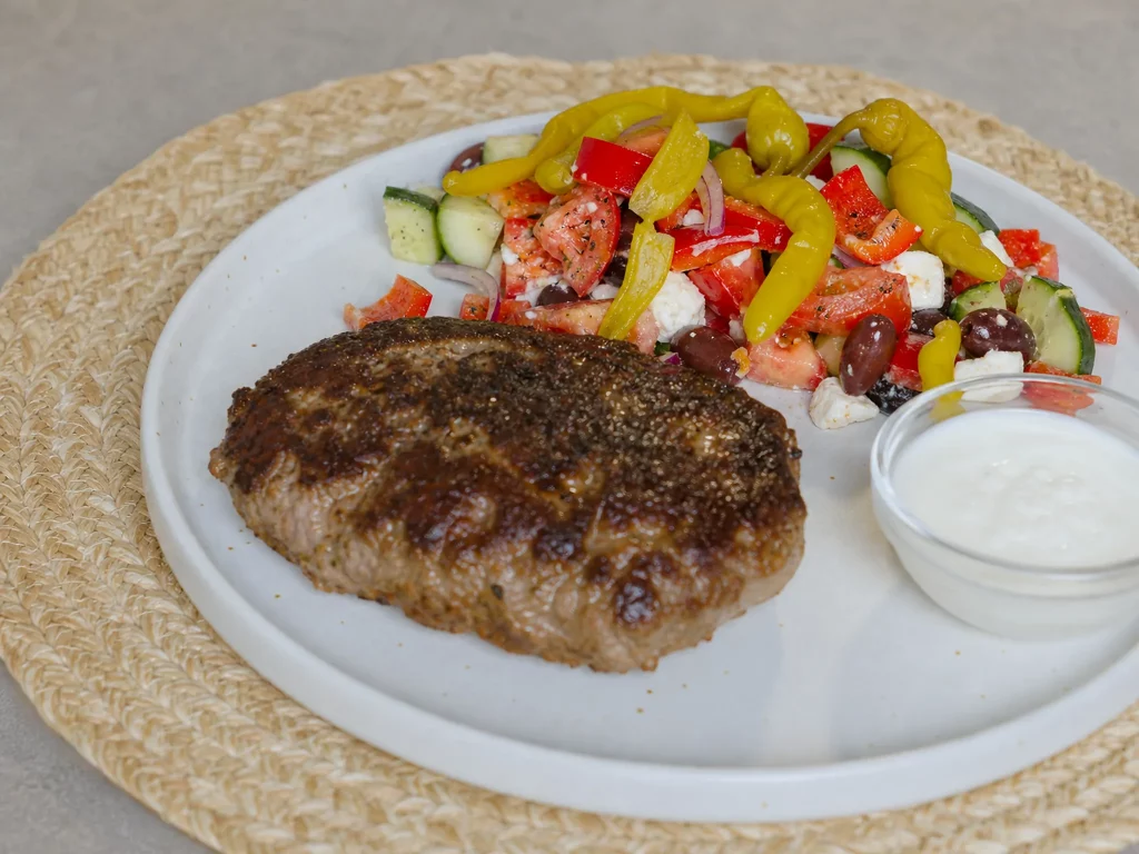 Bifteki mit griechischem Bauernsalat und Knoblauchsoße auf einem Teller angerichtet