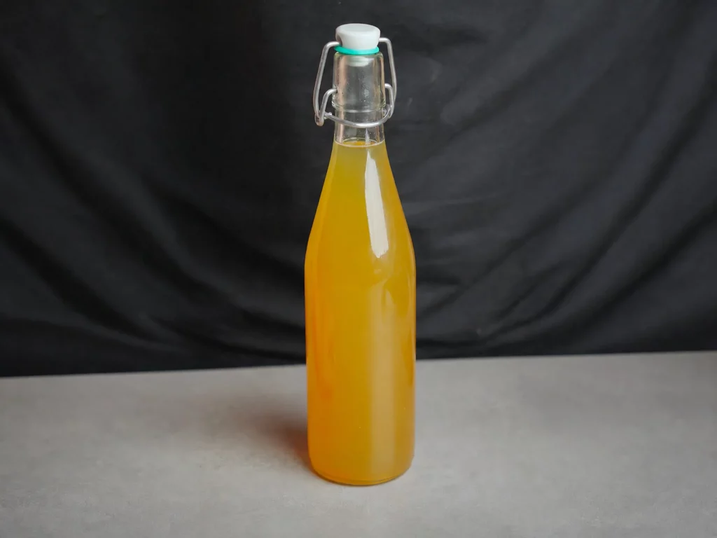 Bratapfellikör in bauchiger Bügelverschluss-Flasche mit goldgelber Farbe, freigestellt vor dunklem Hintergrund