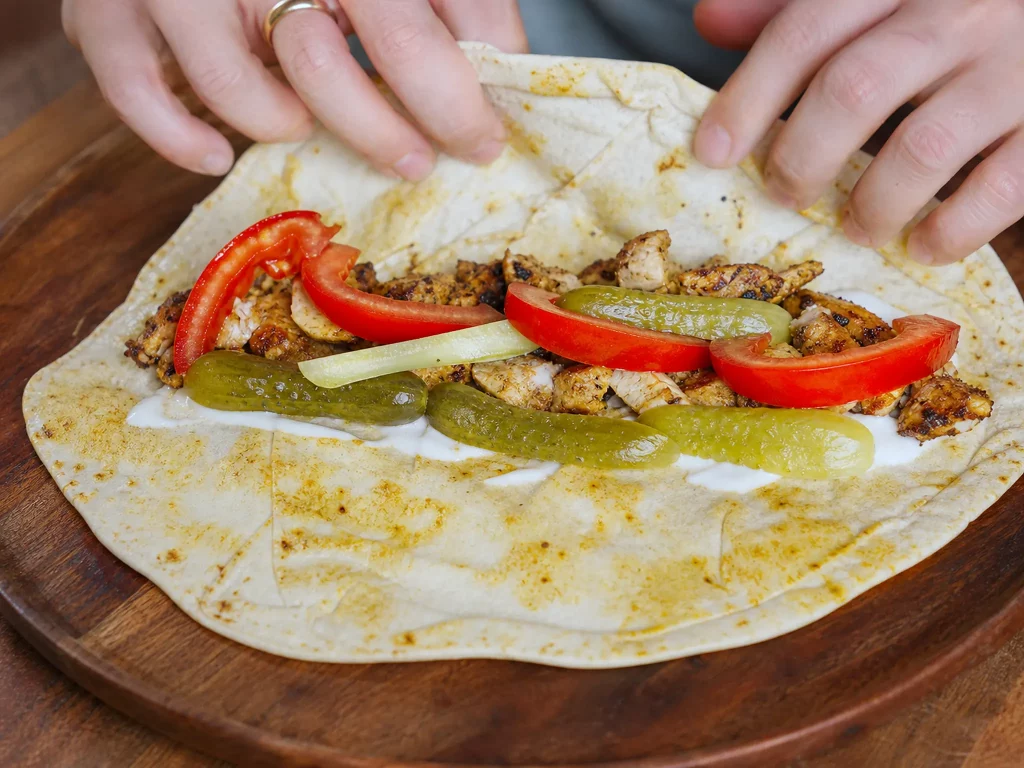 Chicken Shawarma Wrap offen mit Hähnchen, Tomaten und Gewürzgurken beim Belegen