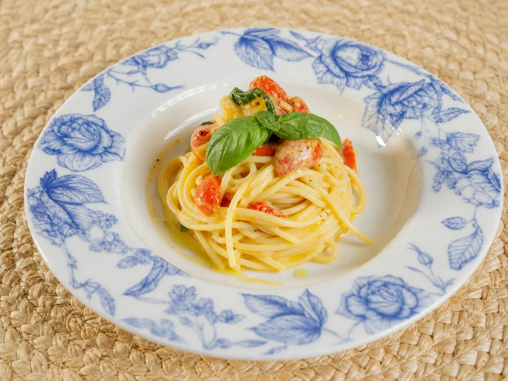 Cremige Tomaten-Burrata-Spaghetti mit Kirschtomaten und Basilikum auf blau-weißem Teller