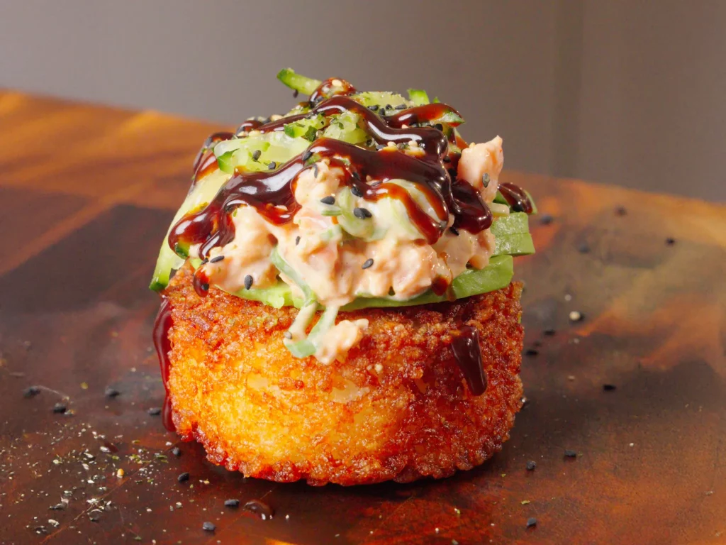 Crispy Sushi Rice Bites – frittierter Sushi-Reis-Taler mit Lachstopping, Gurke und Hoisin, seitliche Nahaufnahme