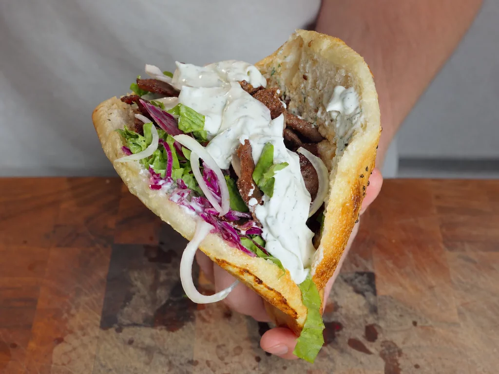 Döner mit alles – aufgeschnittenes Fladenbrot in der Hand, gefüllt mit Fleisch, Rotkohl, Salat, Zwiebeln und Joghurt-Kräutersoße