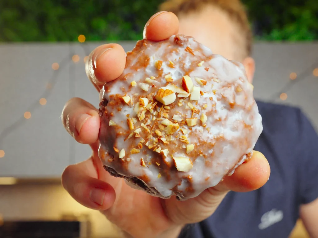 Schoko-Lebkuchen mit weißem Zuckerguss und gehackten Mandeln in der Hand, Nahaufnahme