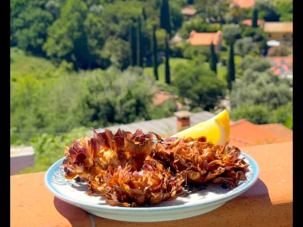 Frittierte Artischocken – knusprig frittiert mit Zitronenspalte auf Teller, Terrassen-Ausblick im Hintergrund