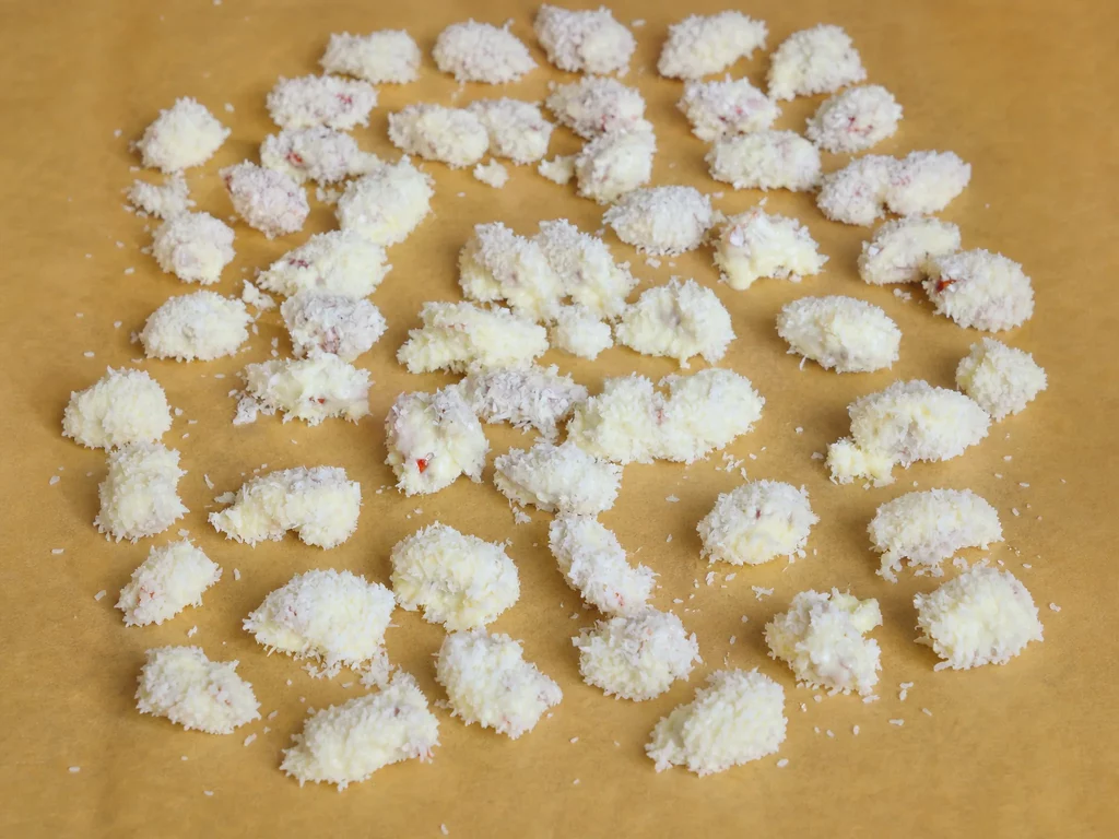 Gebrannte Raffaello-Mandeln mit Kokosraspeln auf Backpapier, mehrere Stück