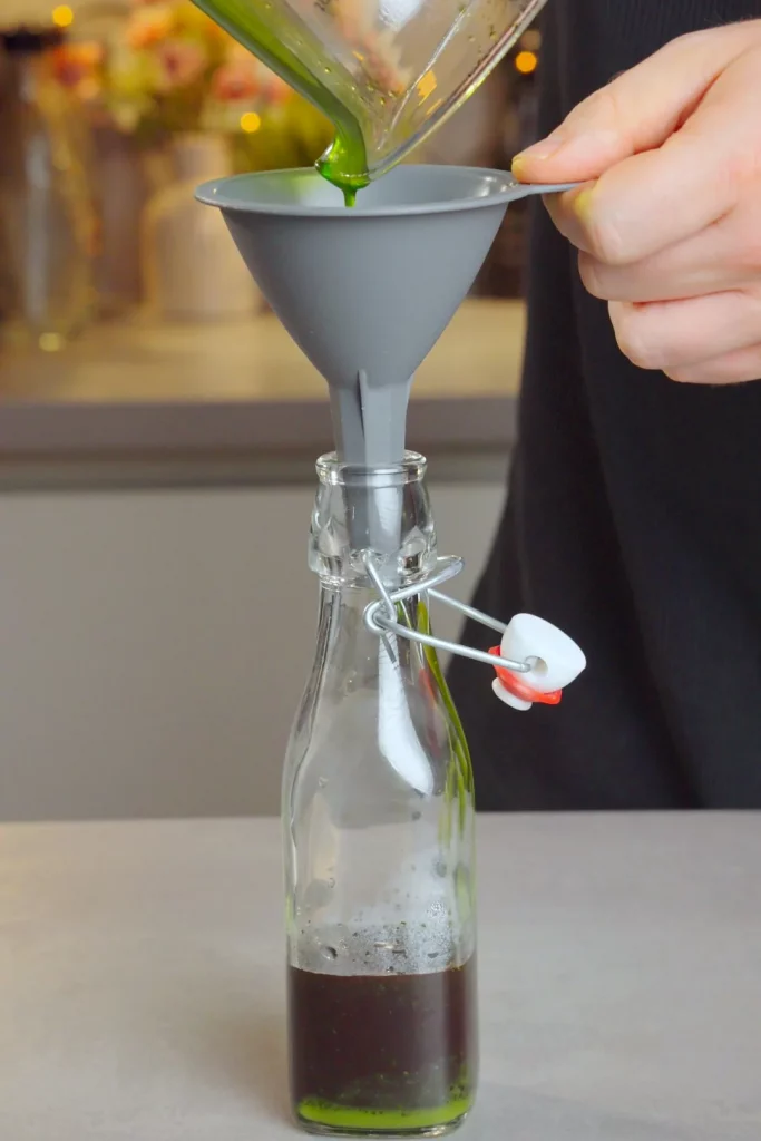 Grünes Kräuteröl wird durch einen Trichter in die Flasche gegossen