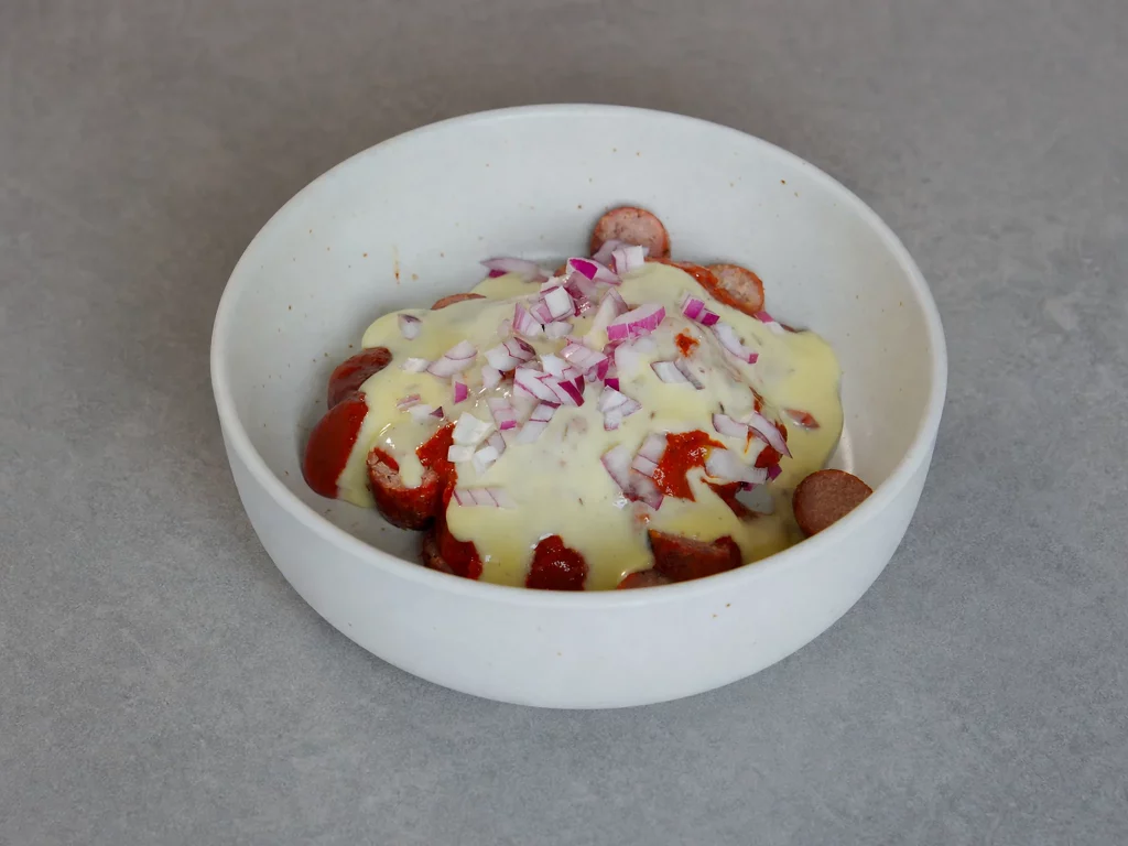 Hessische Currywurst mit Kochkäs – Bratwurst mit Currysauce, Kochkäse und roten Zwiebeln in weißer Schale