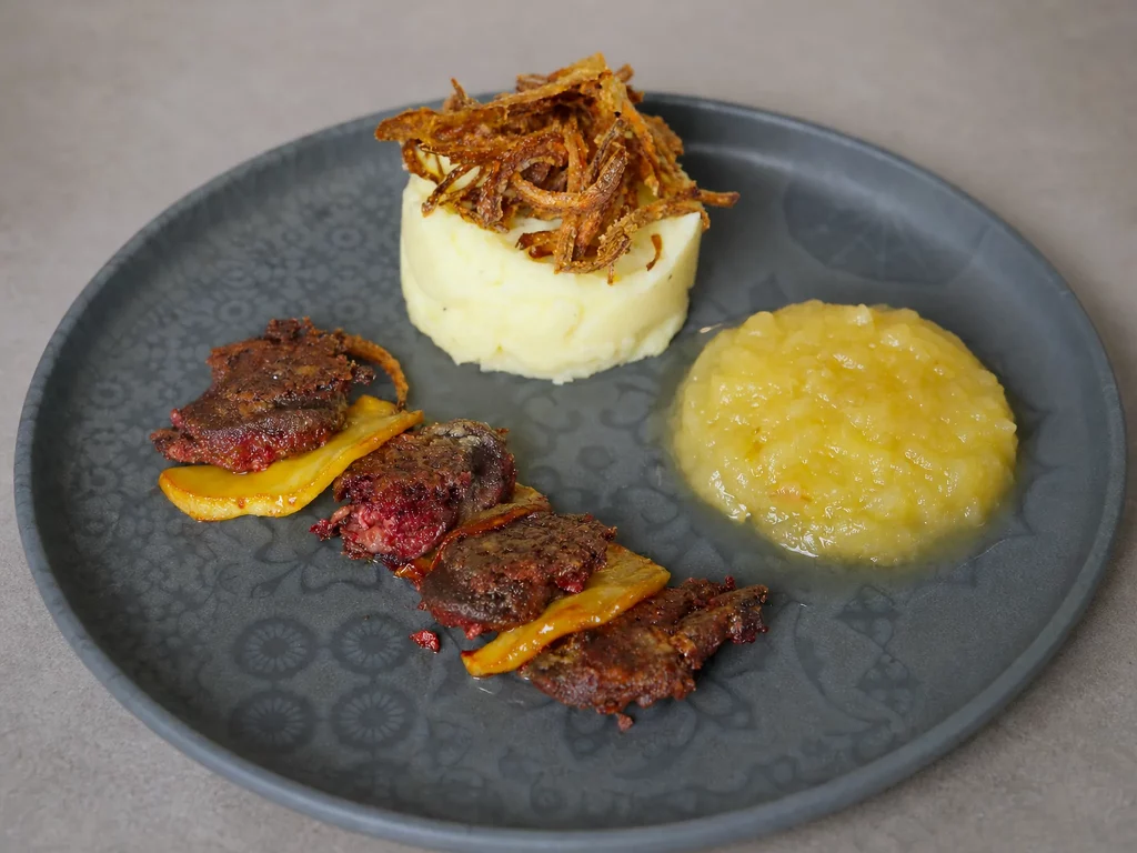 Himmel und Erd – Kartoffelstampf mit Röstzwiebeln, Blutwurst und karamellisierten Apfelscheiben auf grauem Teller