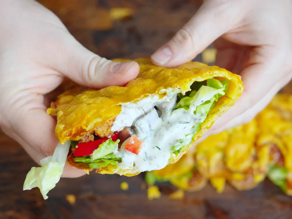 Kartoffel-Wrap mit Fried Chicken, Krautsalat, Paprika und cremiger Dip-Sauce, aufgeschnitten in der Hand gehalten