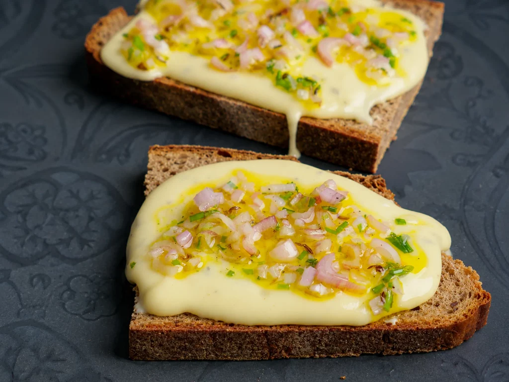Kochkäse mit Mussig – zwei Scheiben Brot mit geschmolzenem Kochkäse und mariniertem Zwiebel-Topping