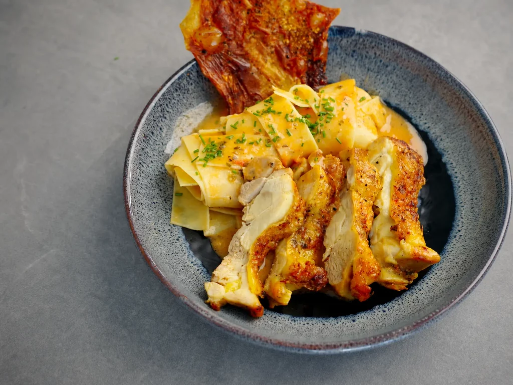 Lorbeerhuhn Toskana mit knuspriger Hähnchenbrust, Pappardelle in cremiger Soße, Schnittlauch und knusprigem Chip in grauer Schale
