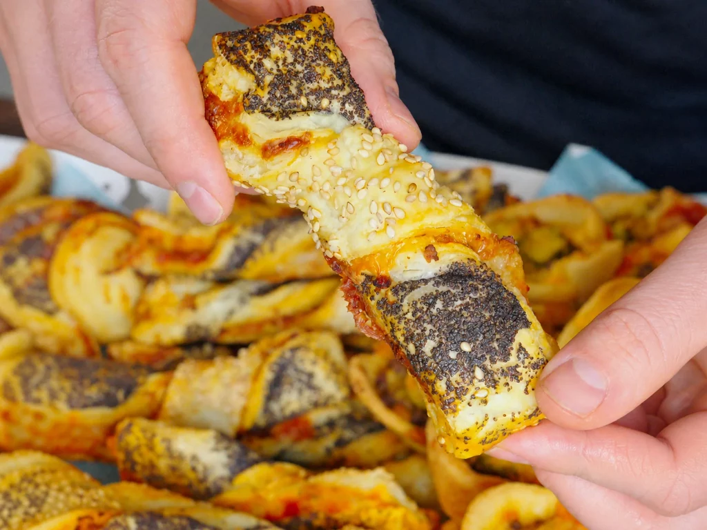 Mini Knusperstangen mit Mohn, Sesam und Käse-Tomaten-Füllung, in der Hand gehalten