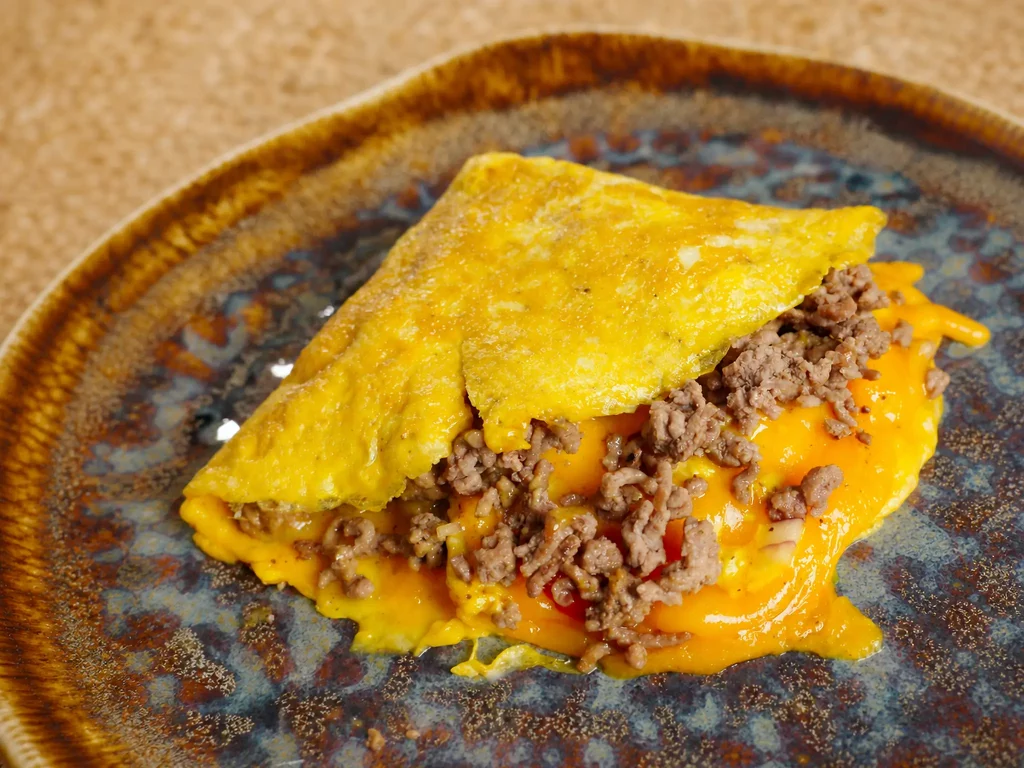 Omelette-Wrap Cheeseburger-Style, gefüllt mit Hackfleisch und geschmolzenem Cheddar, auf blauem Keramikteller