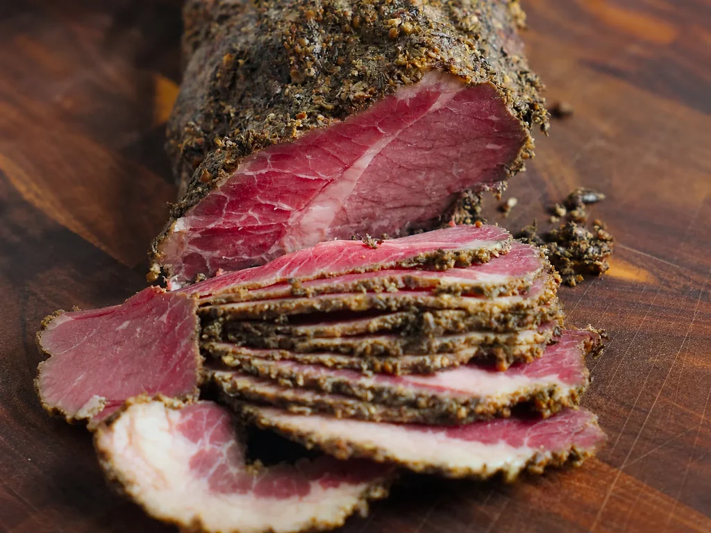 Selbstgemachtes Pastrami mit dunkler Gewürzkruste, in dünne Scheiben geschnitten auf Holzbrett