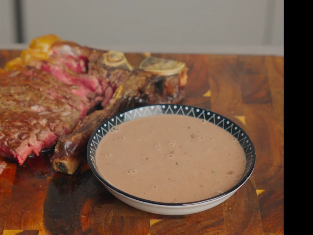 Cremige Pfannen-Steak-Soße in dunkler Schale neben gebratenem Steak