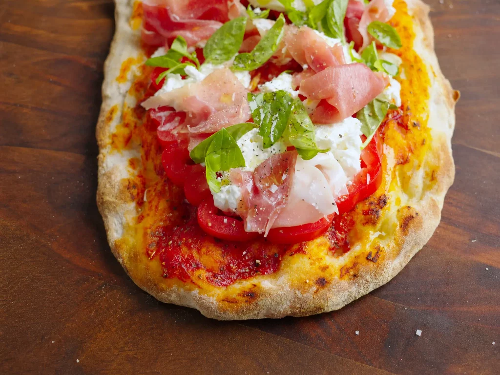 Pinsa mit Tomaten, Prosciutto und Burrata – knusprige Pinsa mit Tomatenscheiben, Burrata, Prosciutto und Basilikum, Nahaufnahme