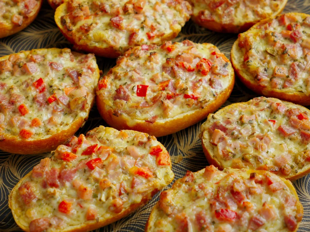 Pizzabrötchen mit Schinken, Paprika und Käse überbacken, mehrere Stück auf Servierplatte