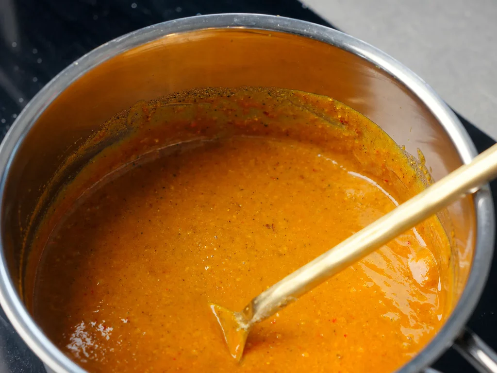 Selbstgemachte BBQ-Soße köchelt glänzend-orange im Topf, mit Löffel verrührt