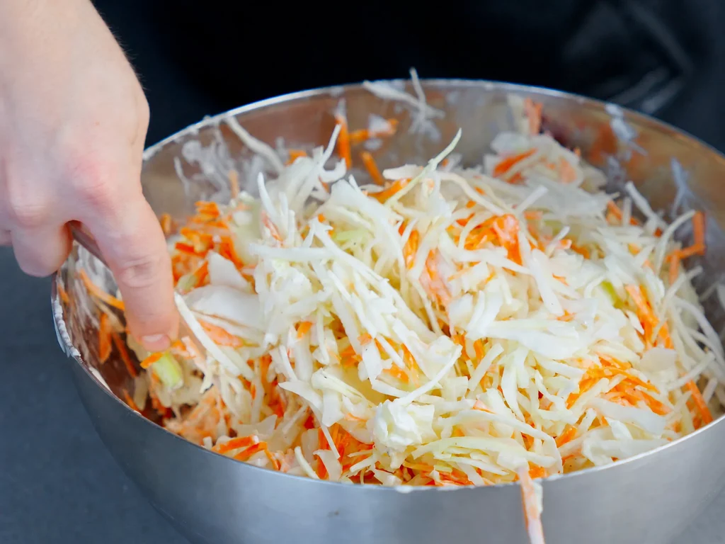 Frischer Cole Slaw aus Weißkohl und Karotten wird von Hand in einer Edelstahlschüssel vermengt