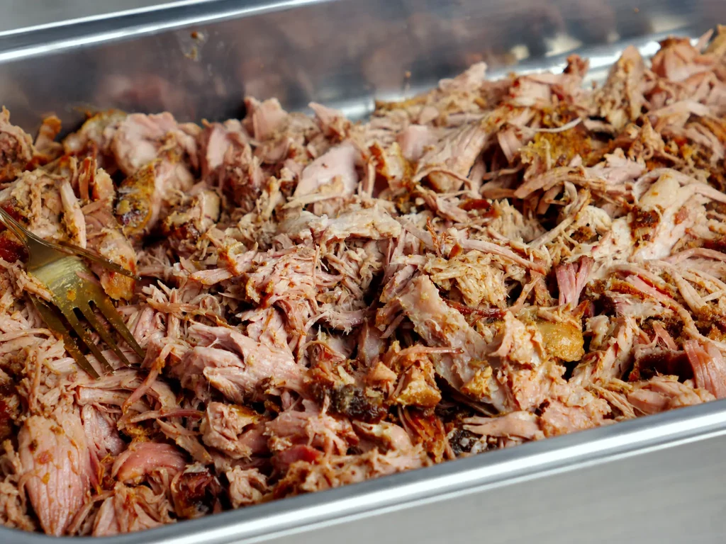Saftig zerzupftes Pulled Pork in einer Edelstahlwanne mit goldener Gabel