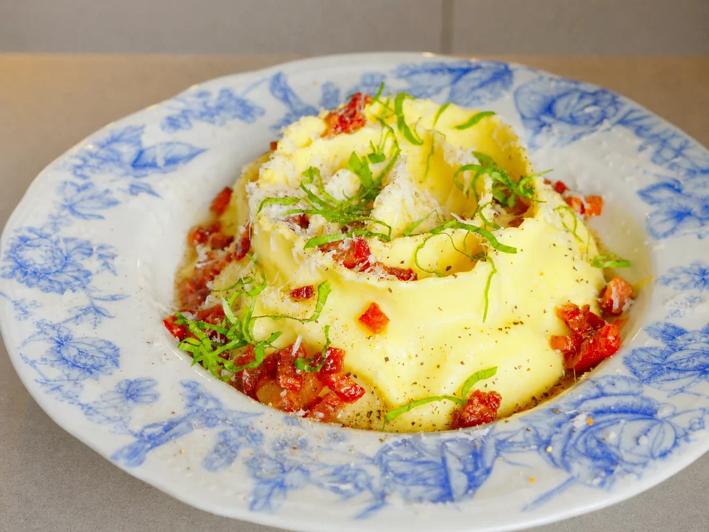 Ravioli-Schnecke mit Cacio e Pepe und Guanciale-Soße – aufgerollte Pasta mit Guanciale-Soße und Pecorino auf blau-weißem Teller
