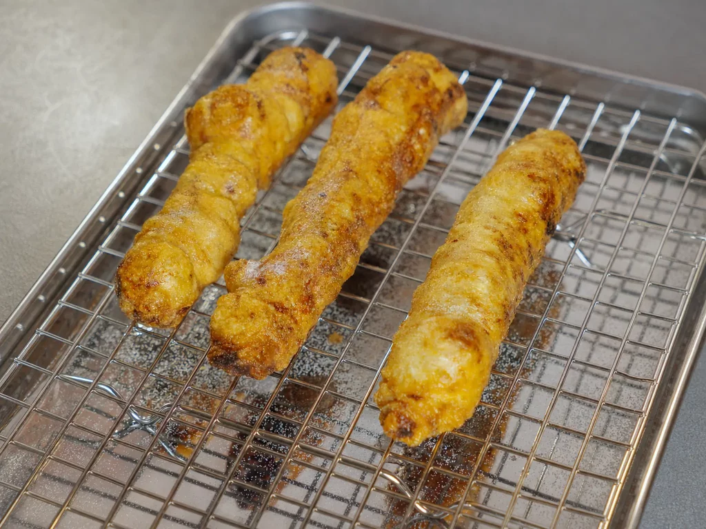 Reispapier-Churros goldbraun und knusprig frittiert, drei Stück nebeneinander auf einem Kuchengitter