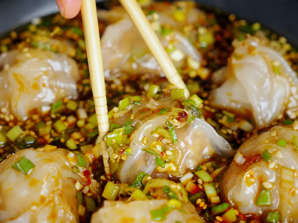 Reispapier Gedämpfte Dumplings mit glasiger Hülle, Soja-Chili-Sauce, Frühlingszwiebeln und Sesam, mit Stäbchen aufgenommen