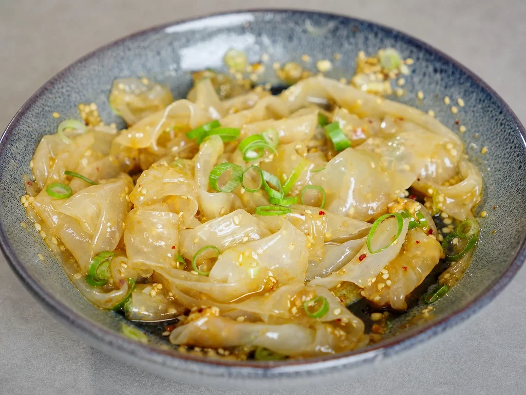 Reispapier-Nudeln in glänzender Sesam-Chili-Sojasauce mit Frühlingszwiebeln in einer Keramikschale