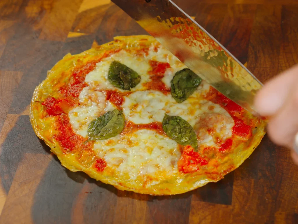 Reispapier-Pizza Margherita mit Tomatensauce, geschmolzenem Mozzarella und Basilikum, wird angeschnitten