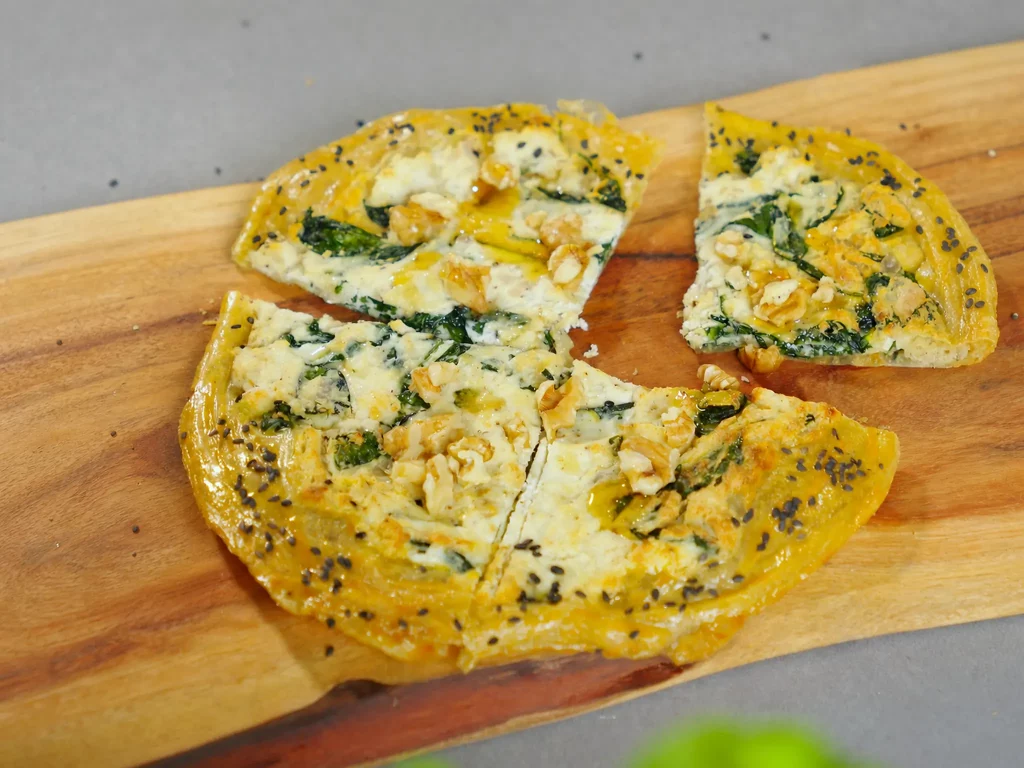 Reispapier Ricotta-Spinat-Tarte mit Walnüssen und schwarzem Sesam, in Stücke geschnitten auf Holzbrett