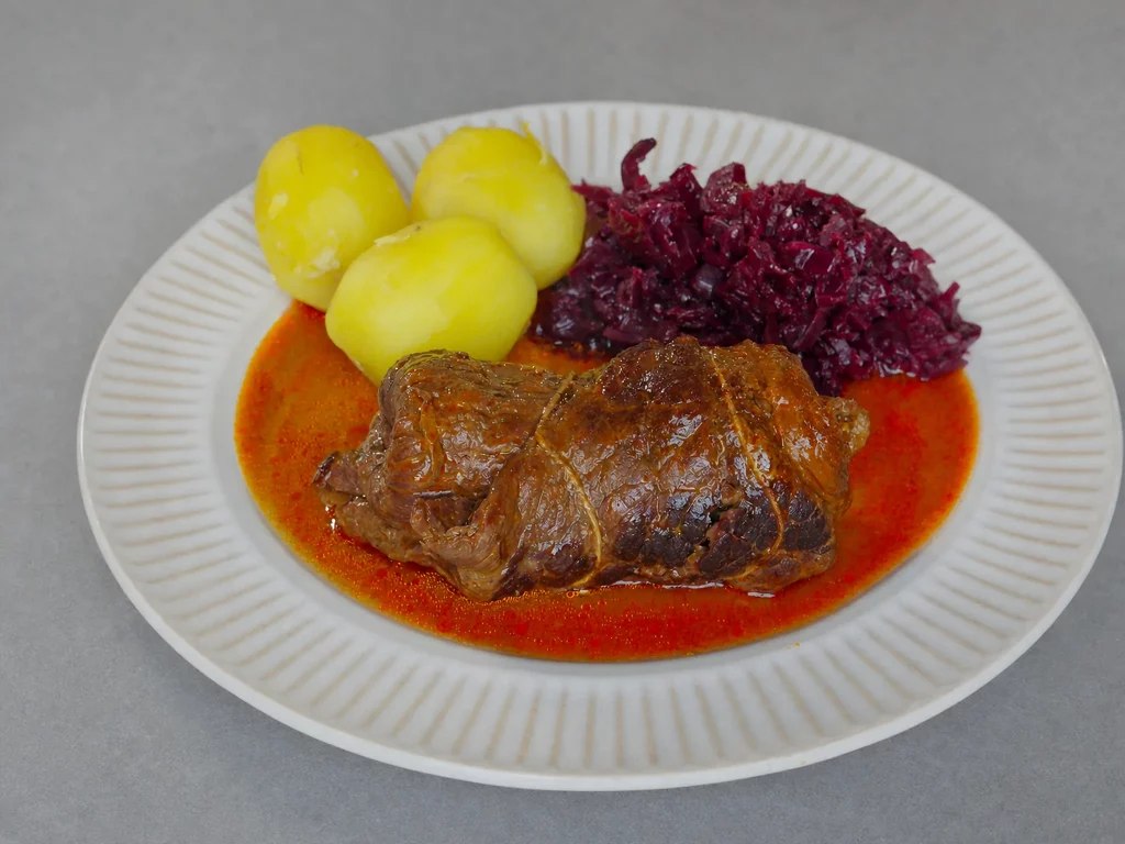Rouladen – Rinderroulade in Bratensauce mit Salzkartoffeln und Rotkohl auf weißem Teller