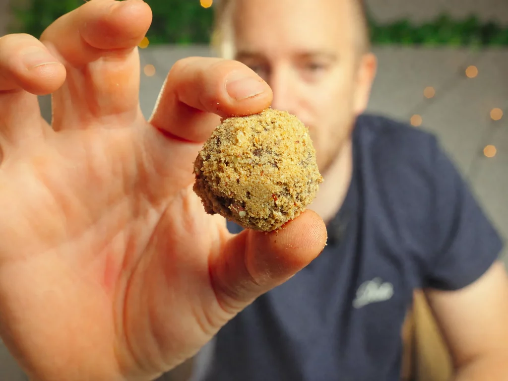 Spekulatius-Kugel in Krümelhülle, zwischen zwei Fingern gehalten