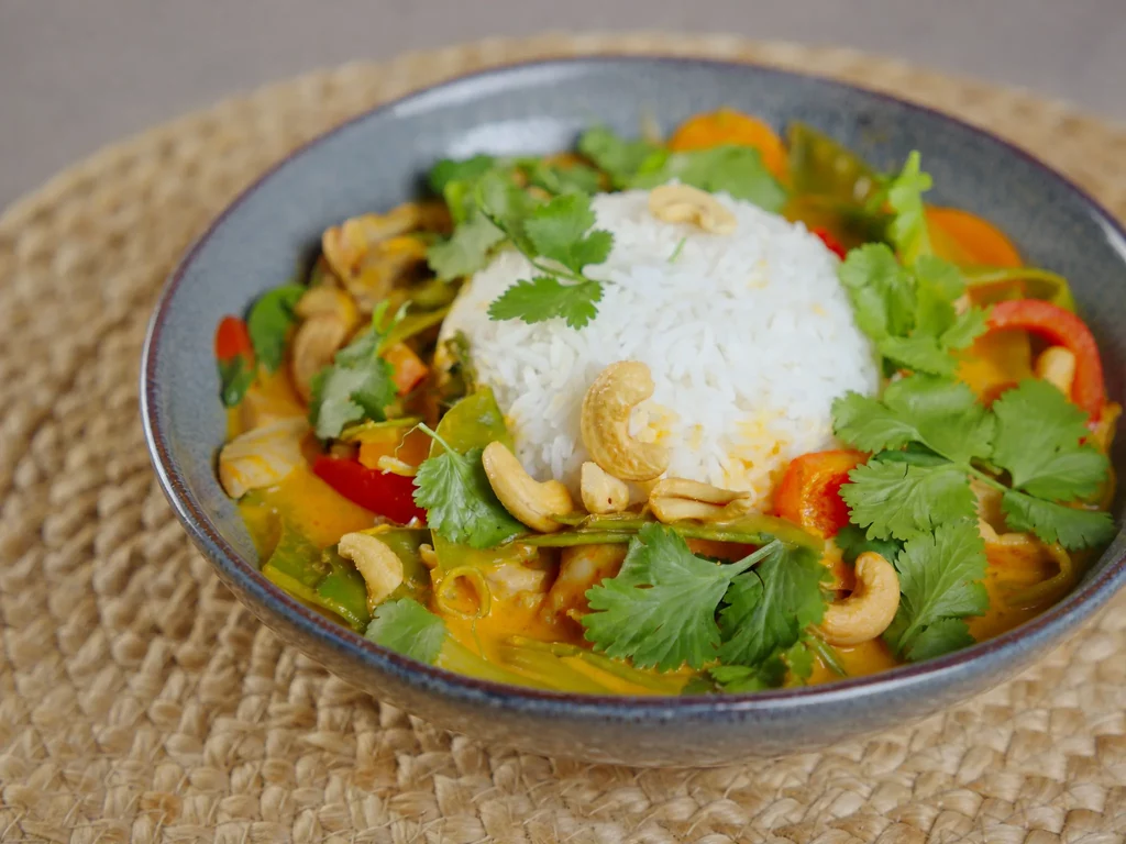 Thai Curry mit Hähnchen, Gemüse, Cashewkernen, Koriander und Reis in blauer Schale