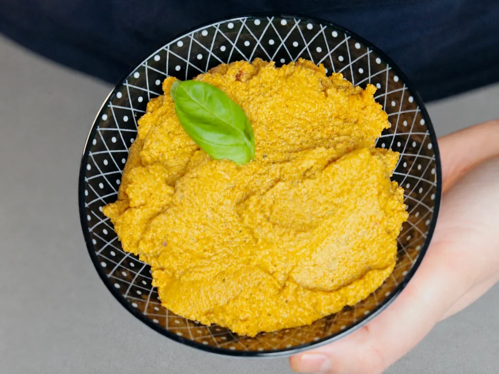 Tomaten Tofu Dip in gepunkteter schwarzer Schale mit Basilikumblatt garniert, in der Hand gehalten
