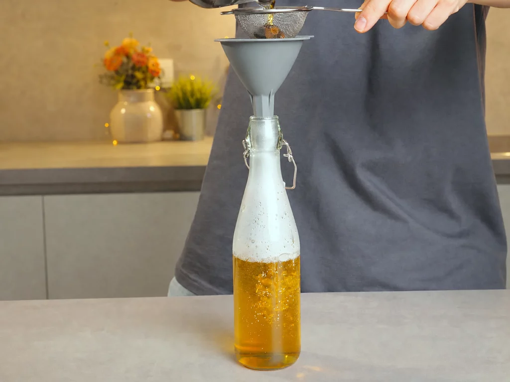 Tonkabohnen-Sirup wird durch ein Sieb in eine Glasflasche abgefüllt