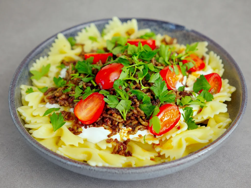 Türkische Pasta mit Farfalle, Joghurt, gewürztem Hackfleisch, Kirschtomaten und Petersilie in grauer Steingutschale