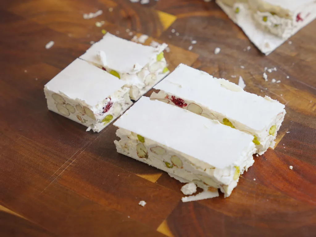 Weißer Nougat mit Mandeln, Pistazien und Cranberries, in Riegel geschnitten auf Holzbrett